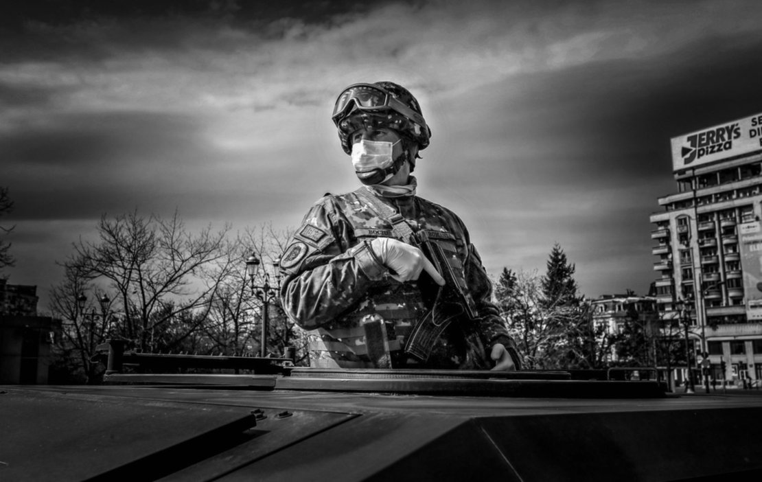 Un soldado rumano con barbijo vigila desde un vehículo militar, mientras la policía realiza controles a los autos de civiles. Un soldado rumano con barbijo vigila desde un vehículo militar, mientras la policía realiza controles a los autos de civiles.